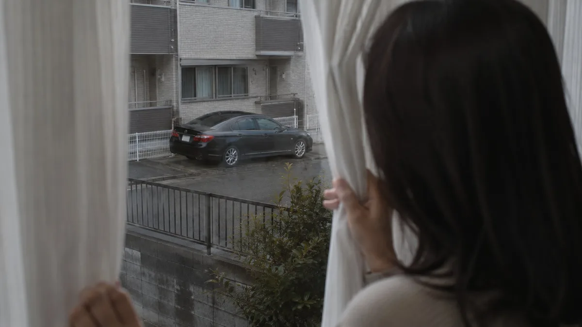 自宅周辺に停まる不審車両をカーテン越しに確認する尾行のサイン