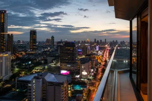 夕暮れのバンコクの高層マンションのベランダから見た都市の街並み、ネオンと車のライトが灯り始める情景、タイの生活環境の変化をイメージした写真
