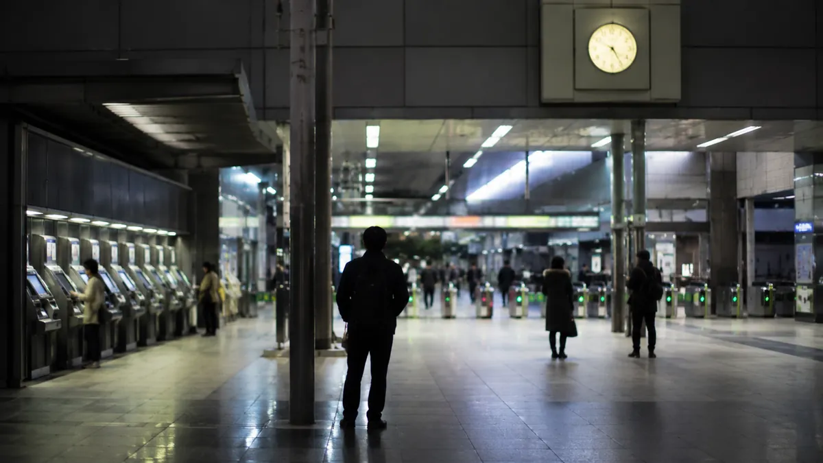 夜の駅コンコースで待つ人と自動券売機の列