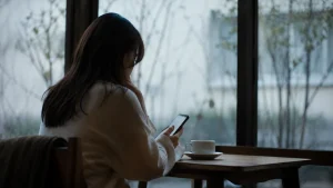 カフェの窓際で一人スマートフォンを見つめる女性の後ろ姿
