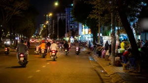 夜のホーチミンの通りを行き交うバイクと歩道の屋台の灯り